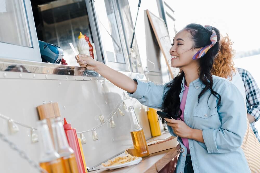 A woman paying for her food at a food truck opened with a business loan