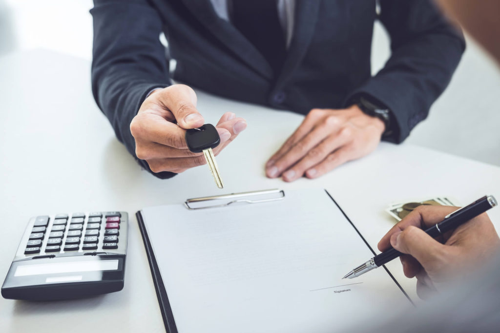 A car dealer handing out a car key as the buyer signs the hire purchase agreement