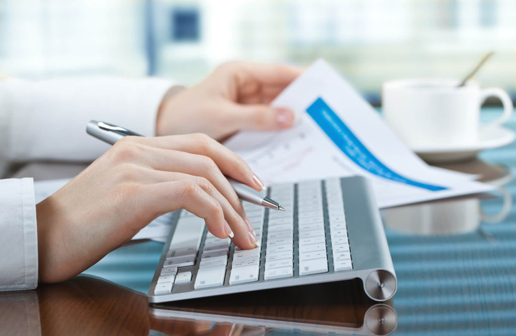 An individual holding a pen and typing on a keyboard