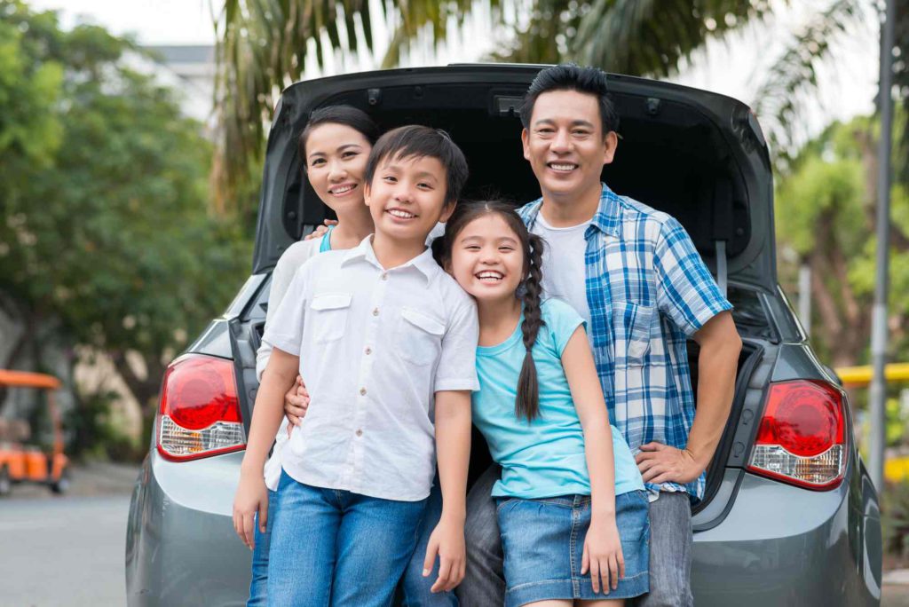 Family standing in front of a car with an open boot, bought with an in-house auto loan