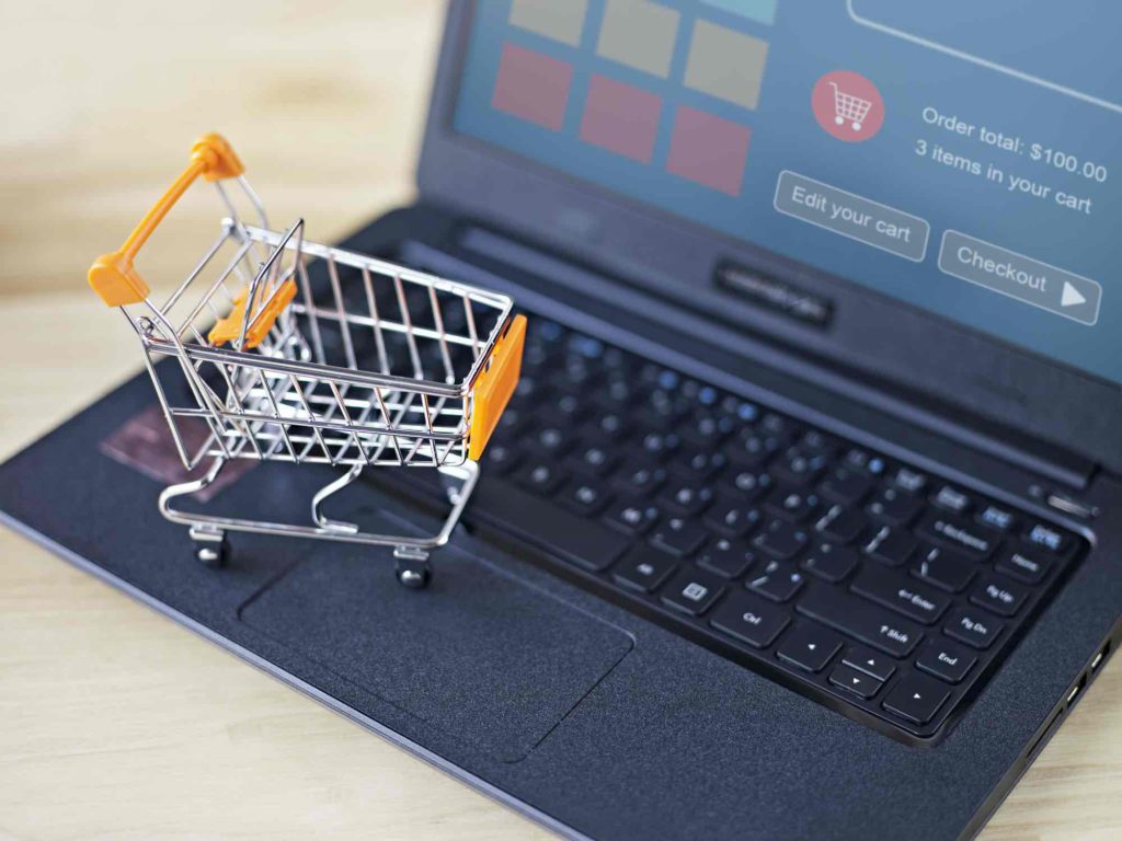 A miniature shopping cart on top of a laptop showing a shopping checkout screen