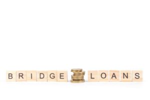 Wooden blocks spelling ‘bridge loans’ with a stack of gold coins in the middle